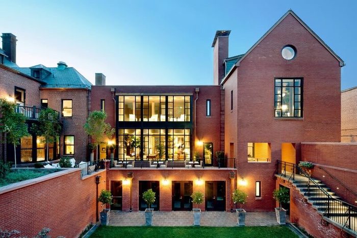 Building features illuminated windows, surrounded by brick architecture, with a courtyard and staircase, under a clear evening sky.