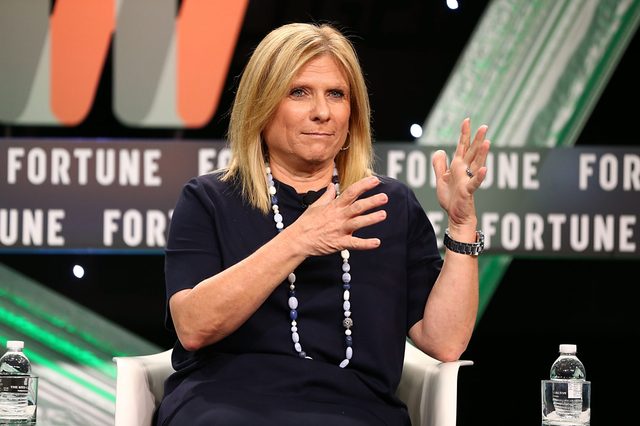 A person gestures while seated, with a "FORTUNE" background and two water bottles on a stage.
