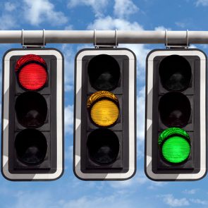 Traffic lights display red, yellow, and green signals, hanging against a blue, partly cloudy sky backdrop.