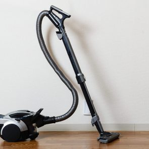 Vacuum cleaner rests against a wall with wooden floor context.