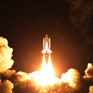 Space shuttle launches, emitting bright flames, surrounded by billowing clouds against a starry night sky.