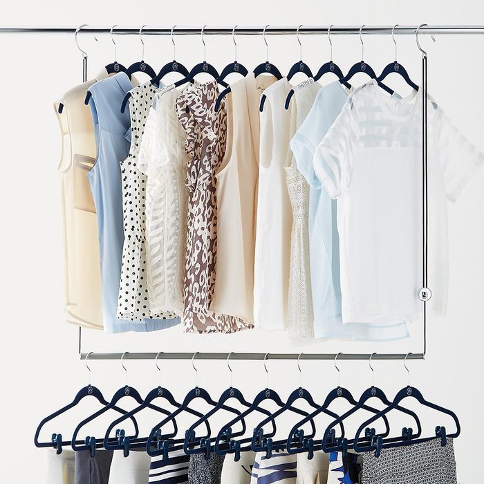Clothes hang on two rows of hangers, displaying various light-colored tops and bottoms. They are organized neatly on a metal rack against a white background.