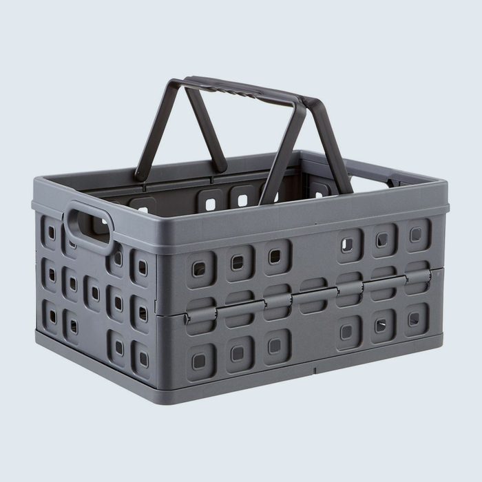A gray plastic basket stands upright with folded handles, featuring square-patterned cutouts, against a plain, light-colored background.