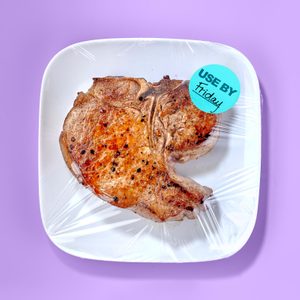 Pork chop packaged on a white plate sealed with plastic wrap; 