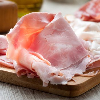 Slices of ham rest on a wooden board in a bright kitchen setting.