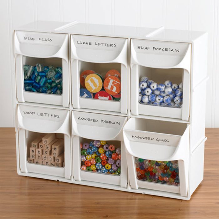Plastic bins hold varied craft items on wood table; labels read 