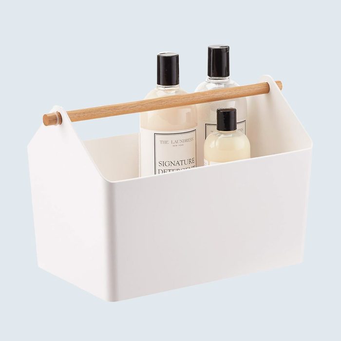White caddy holds bottles, featuring a wooden handle, set against a plain light gray background.