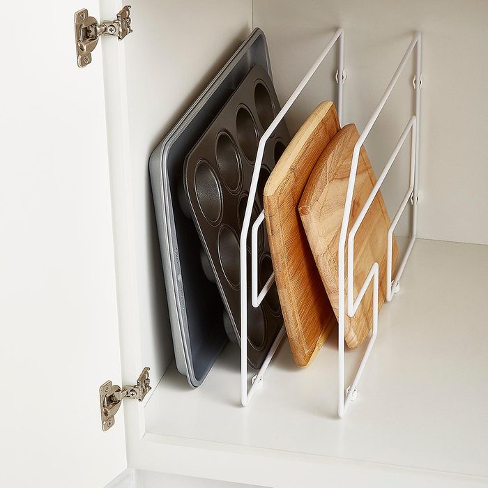 Metal rack holds baking trays and wooden boards in a white cabinet, organized and upright for storage.