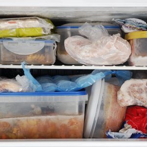Frozen food fills containers and bags on crowded freezer shelves, showcasing a variety of stored items in a home kitchen setting.