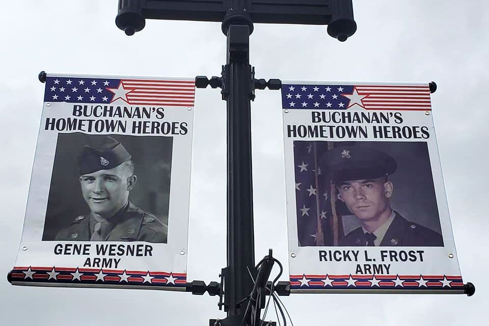 Banners display military portraits labeled "Buchanan's Hometown Heroes," featuring Gene Wesner and Ricky L. Frost, with an American flag design framing the images.