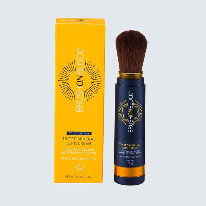Brush applicator dispenses tinted mineral sunscreen beside its orange box. Box reads: 