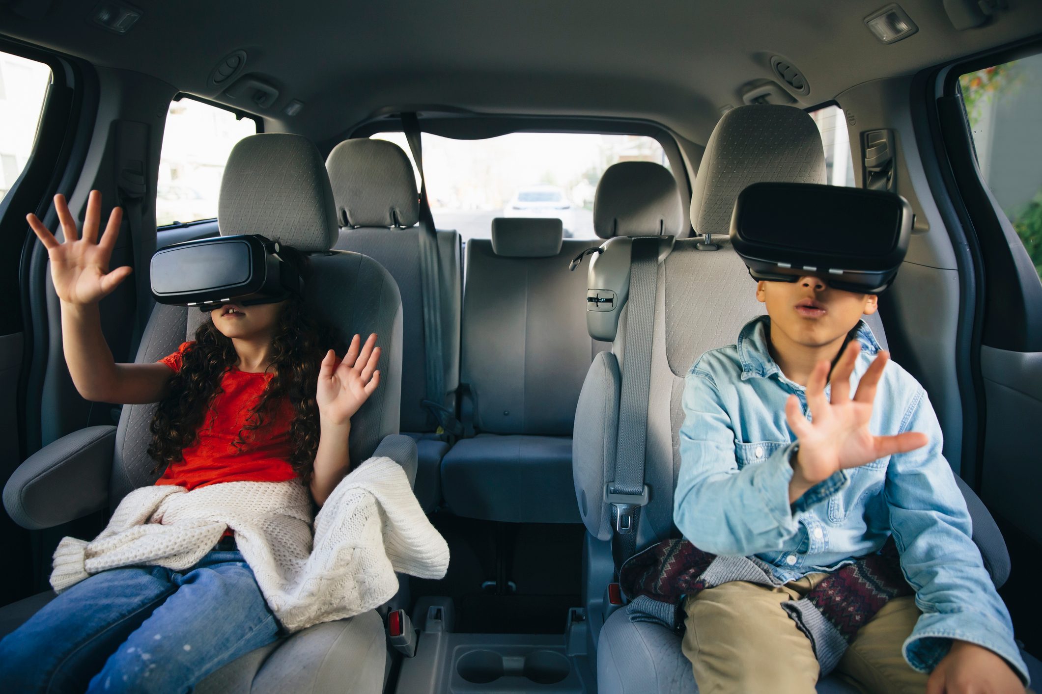 Mixed race children using virtual reality goggles in car
