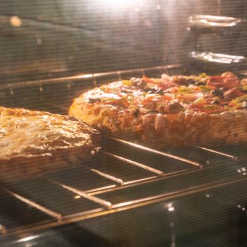Two pizzas bake on an oven rack, melting cheese and toppings. The warm glow illuminates their crusts in the enclosed space.