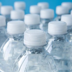 Plastic water bottles, capped, arranged closely together, with a blurred blue background.