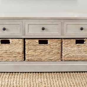 A wooden bench with three drawers above wicker baskets on a woven rug in a room.
