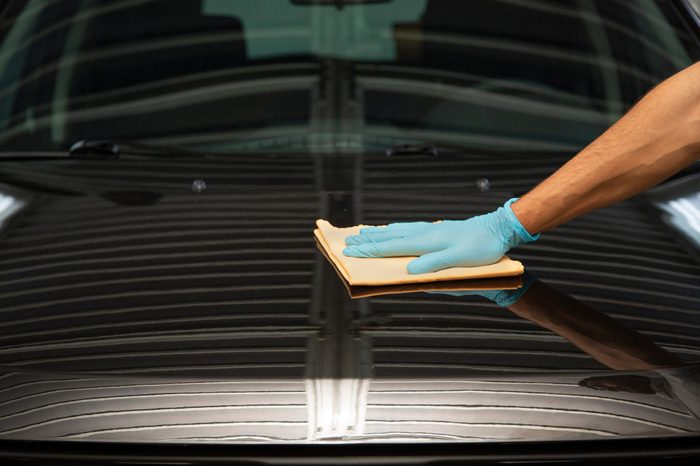 Gloved hand polishes black car hood with a cloth in a well-lit garage.