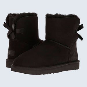 Black boots with bows sit on a light background, showcasing their plush lining and simple design.