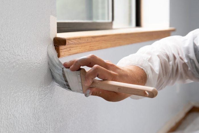 Man painting interior of home by window