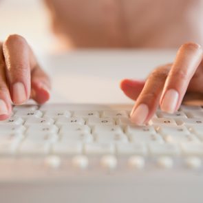 Hands typing on a white keyboard, close-up, with a blurred background.