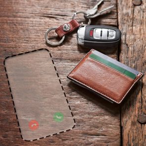 Wallet rests on a wooden surface, beside car keys. An invisible phone outlined with call icons is sketched on the wood.