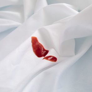Red sauce stain sits on crumpled white fabric background, creating a contrasting visual focal point.
