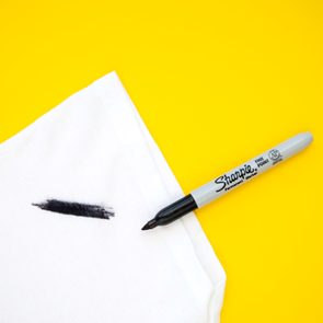 Marker leaves black stain on white fabric, sits on bright yellow background.