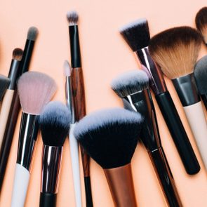 Makeup brushes arranged side by side on a flat, peach-colored background.