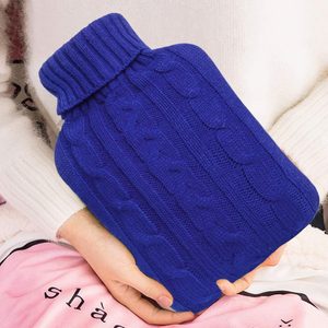 Blue knit hot water bottle, held by hands, rests on a person's lap amidst soft, light-colored fabric.