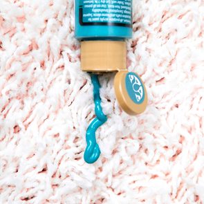 Turquoise paint oozes from a tube onto a white textured fabric.