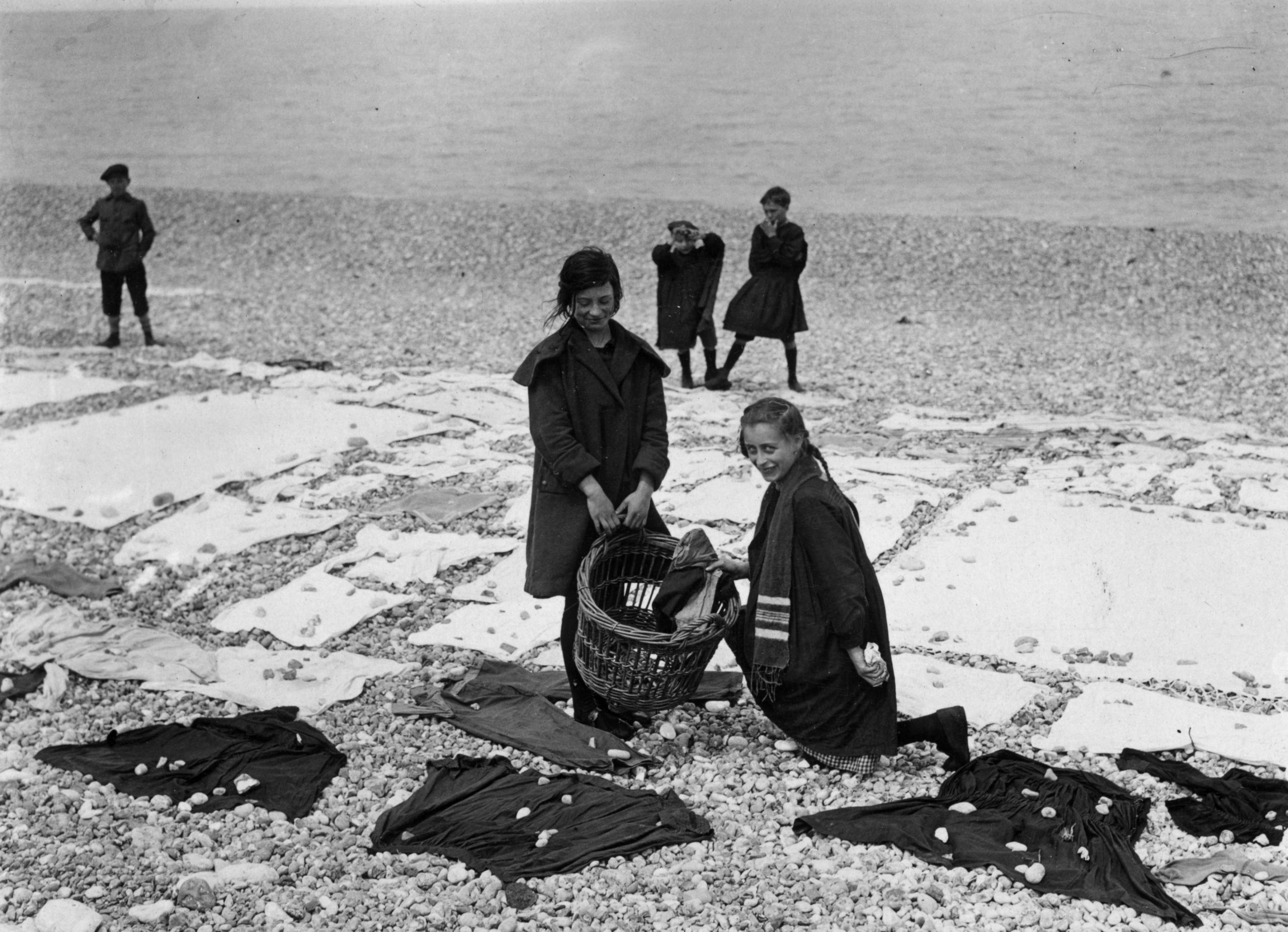 Girls weigh down clothes with pebbles at the beach on washing day