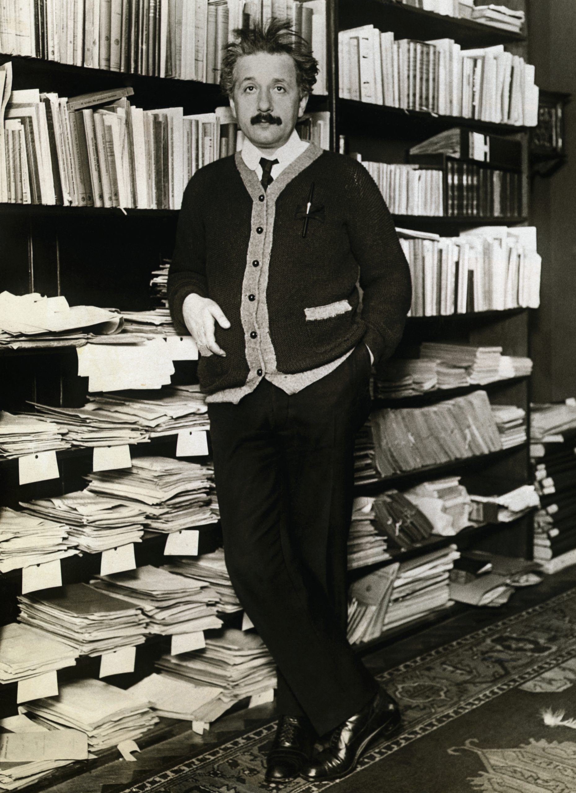 Albert Einstein leaning against shelves of scientific books