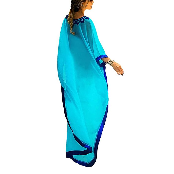 Woman wearing a flowing blue dress walks with one arm extended, adorned with bracelets, against a plain white background.