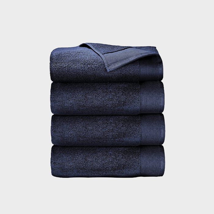 Four neatly stacked dark blue towels rest on a plain, light gray background. The top towel's corner is folded over.