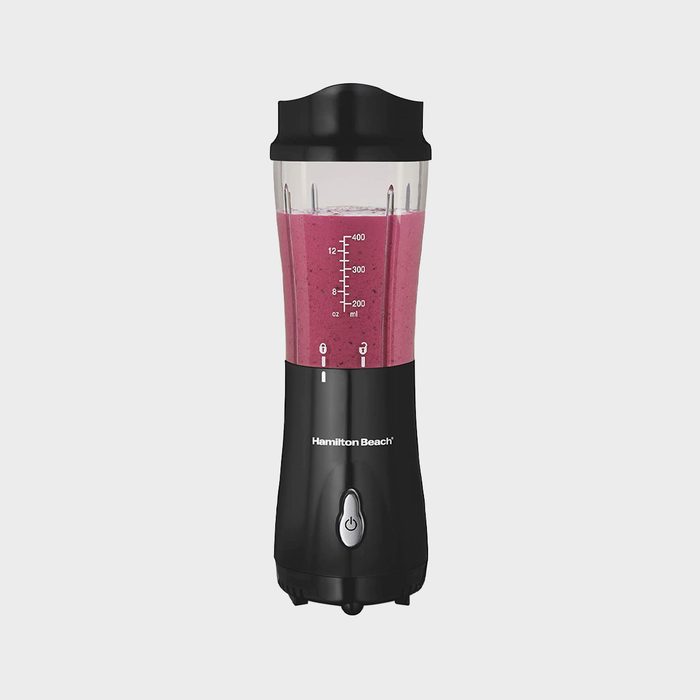 A blender containing a pink smoothie sits on a plain, light gray background; measurement markings and the brand name 