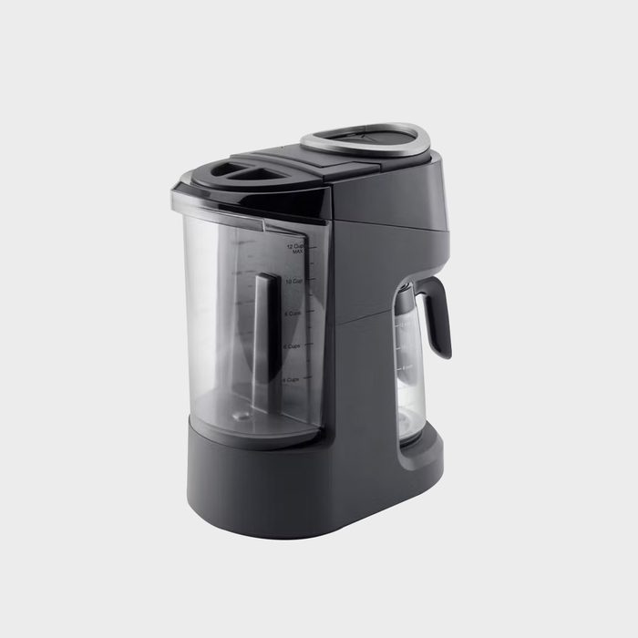 A dark gray coffee maker sits idle, featuring a glass carafe and measuring markings, set against a plain, light gray background.