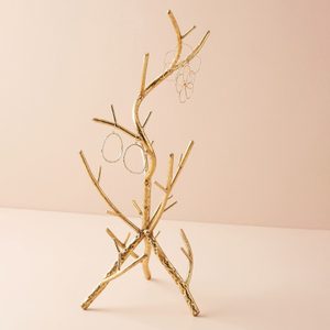 Golden tree-shaped stand displaying earrings stands on a smooth beige surface against a matching background.