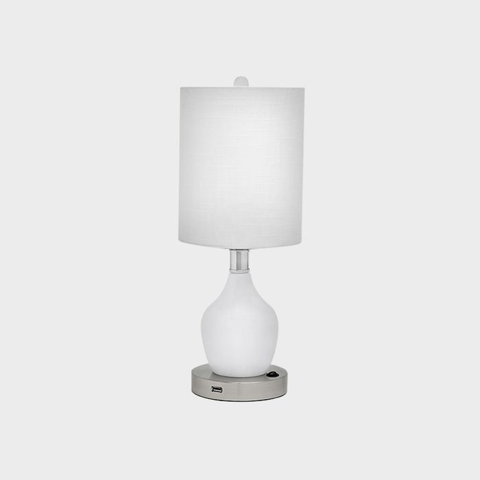 A white table lamp sits on a metallic base with USB ports, against a plain gray background.