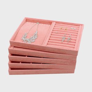 Stacked pink velvet jewelry trays display necklaces and earrings, organized in compartments, against a plain gray background.