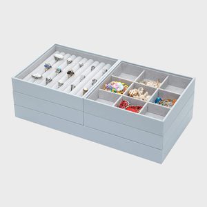 Jewelry organizer displays rings and assorted jewelry; sits on a smooth, stacked tray with compartments, set against a plain, light gray background.