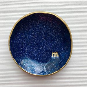 Dark blue, circular dish with gold edge, features subtle sparkles and a lowercase 