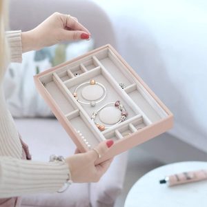 A jewelry box holding bracelets and rings is being organized by a person in a cozy room with a chair and table nearby.