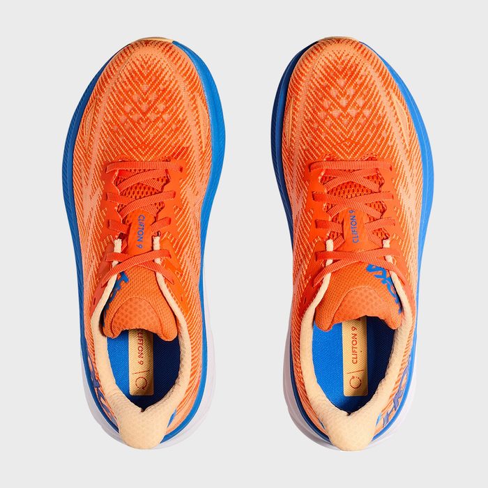 Bright orange running shoes with blue accents, viewed from above, resting on a neutral surface. The insoles read 