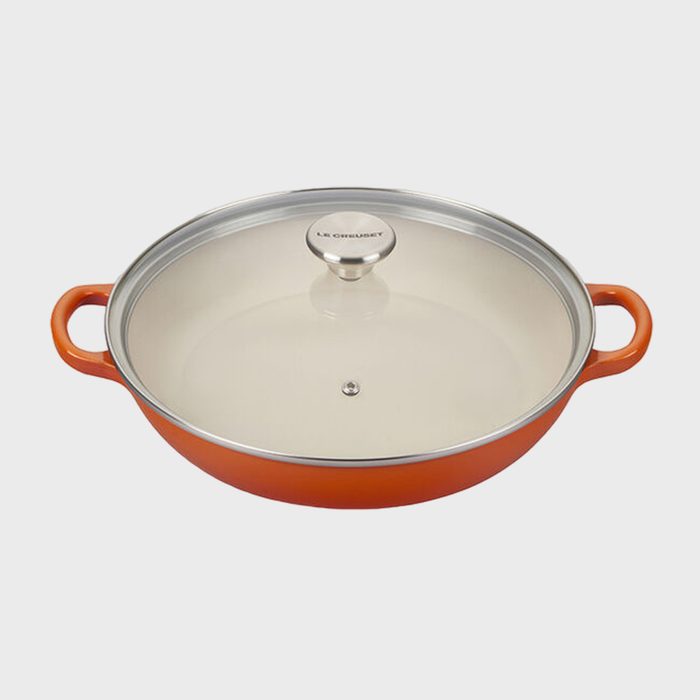 Orange cast iron skillet sits with a glass lid, featuring two handles, against a plain background; text reads 