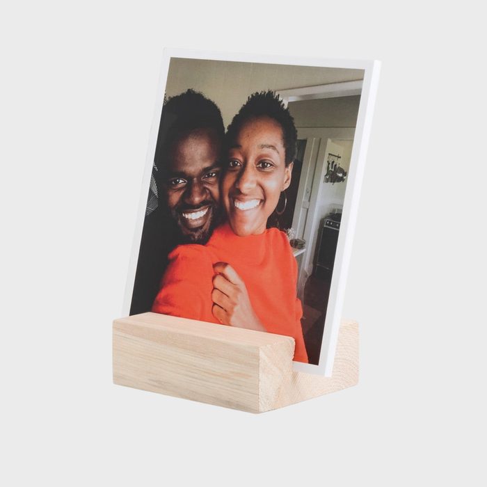 Photo in wooden stand showing two people smiling, indoors, with neutral background.