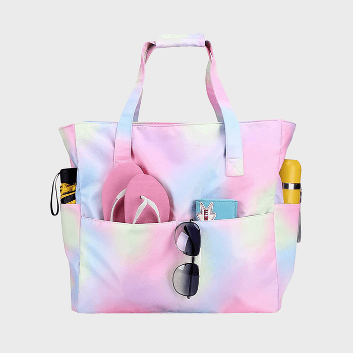 Pastel tote bag holds sunglasses, flip-flops, and small items in outer pockets, against a plain gray background.