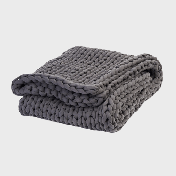A chunky, gray knitted blanket is folded neatly against a plain white background.