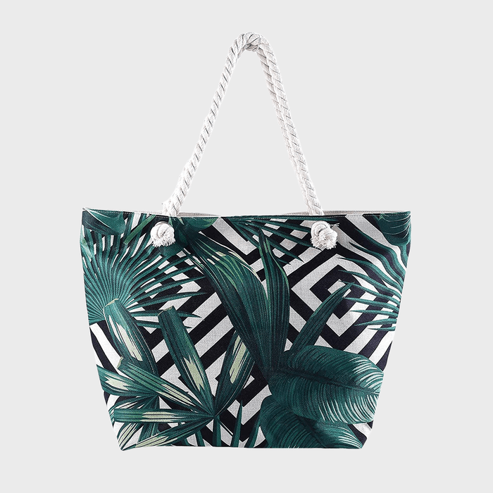 Tropical-patterned tote bag hangs with rope handles, featuring large green leaves against a geometric black-and-white background.