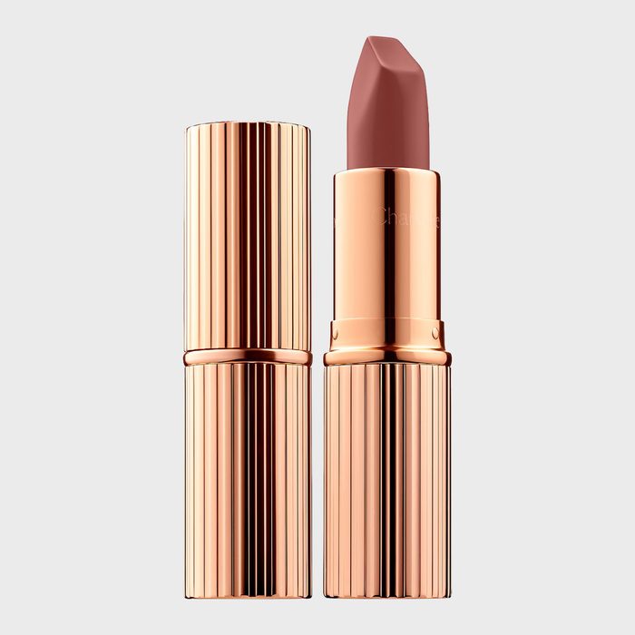 Gold lipstick tube standing open, revealing a mauve lipstick bullet against a plain, light gray background.