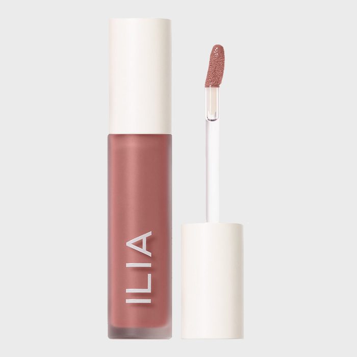 Lip gloss bottle stands open; applicator shows pink shade. White cap detached. Text reads 