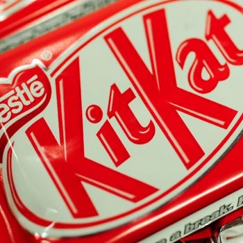 A KitKat wrapper displays bold red and white branding with "NestlÃ© KitKat." It rests among other similar wrappers, emphasizing brand identity.